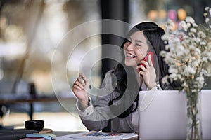 Attractive young asian business woman talking on the mobile phone and smiling while sitting at her working place in office