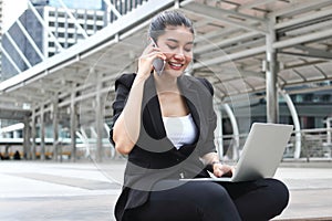 Attractive young Asian business woman working with laptop and mobile smart phone at outside office
