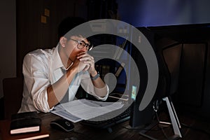Attractive young asian businessman concentrated working until late overtime on publication at his desk in dark modern office at