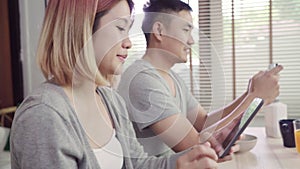 Attractive young Asian couple distracted at table with newspaper and cell phone while eating breakfast.