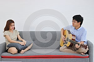 Attractive young Asian couple playing acoustic guitar together in living room. Love and romance people concept