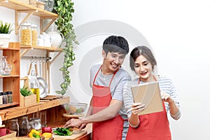 Attractive young asian couple or student looking at recipe and enjoy cooking food in kitchen at home. Man and woman in gen