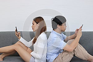 Attractive young Asian couple using mobile smart phone together in living room. Internet technology lifestyle concept