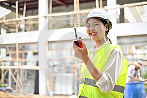 Attractive young Asian female engineer using a walkie talkie in the construction site