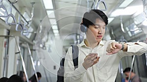 Attractive young Asian man watching video clip from Internet using his mobile phone while keep checking time on the watch