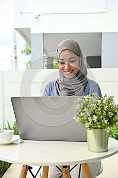 Attractive young Asian Muslim woman remote working at home, using laptop