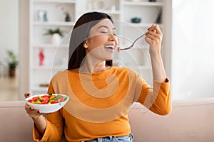 Attractive young asian woman eating vegetable salad at home