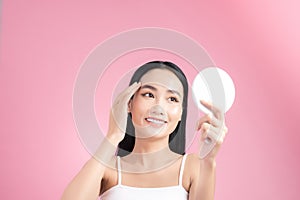 Attractive young Asian woman holding mirror and feeling happy about her skin.  on pink background