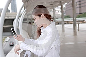 Attractive young Asian woman looking on mobile smart phone in her hands at building urban background.