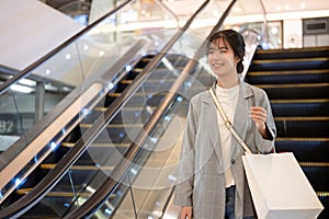 An attractive young Asian woman with shopping bags is going down an escalator in a shopping mall