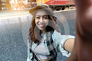 Attractive young Asian woman traveler with backpack taking a photo or selfie in train station. Travel lifestyle concept