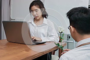 Attractive young Asian woman working with laptop with business man giving a white rose in office on valentine`s day. Love and rom