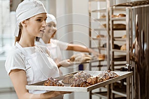 attractive young baker holding tray with fresh croissants