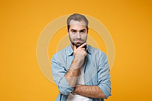 Attractive young bearded man in casual blue shirt posing isolated on yellow orange background studio portrait. People