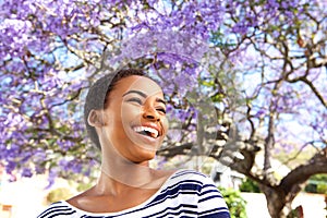 Attractive young black woman laughing outdoors by flower tree