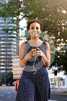Attractive young black woman walking in city with mobile and earphones