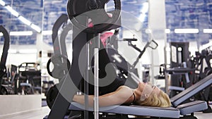 Attractive young blond caucasian woman with sporty body smiling while exercising on leg press mashine at the gym