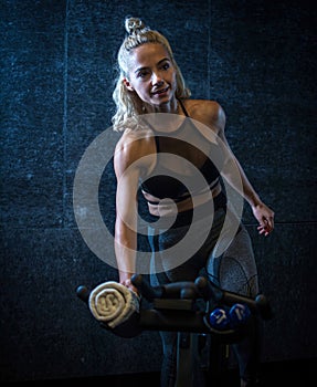 Attractive young blond haired woman in sportswear riding stationary indoor bike