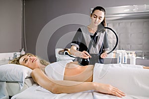 Attractive young blond woman client with slim fit body getting anticellulite and anti fat therapy in beauty salon on her
