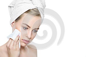 Attractive young blond woman with her hair wrapped in a towel, removing make up using soft face wipe.