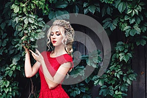 Attractive young blonde girl in red dress posing near a wild vineyard.