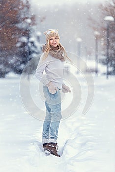 Attractive young blonde girl walking in winter forest. Pretty woman in wintertime outdoor. Wearing winter clothes. Knitted sweater