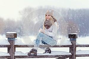 Attractive young blonde girl walking in winter forest. Pretty woman in wintertime outdoor. Wearing winter clothes. Knitted sweater