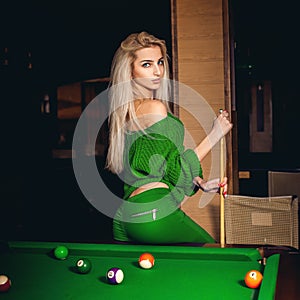 Attractive young blonde lady plays billiard