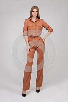 Attractive young blonde model with perfect slim body posing in trendy orange pantsuit full length