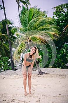 Attractive young blonde woman in bikini standing on sandy beach on windy day