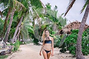 Attractive young blonde woman in bikini standing on sandy beach on windy day