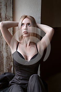 Attractive young blonde woman wears black top with deep sweetheart neckline with her hands behind head. Girl with seductive figure