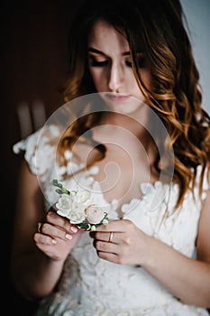 Attractive young bride holding the groom`s buttonhole. flowers with pink roses, white carnation and green and greens. Bride`s