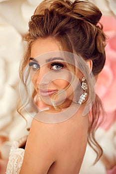 Attractive young bride with makeup and fashion wedding hairstyle. Closeup portrait of young gorgeous woman over roses wall flowers