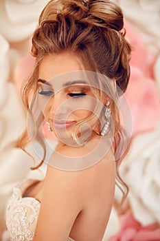 Attractive young bride with makeup and fashion wedding hairstyle. Closeup portrait of young gorgeous woman over roses wall flowers