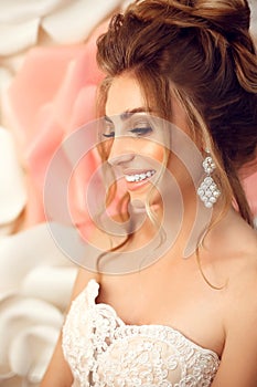 Attractive young bride with makeup and fashion wedding hairstyle. Closeup portrait of young gorgeous woman over roses wall flowers