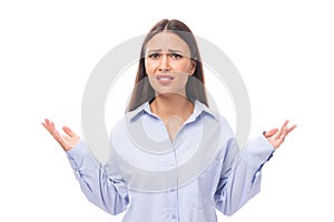 attractive young brunette caucasian woman dressed in a sky blue shirt throws up her hands on a white background with