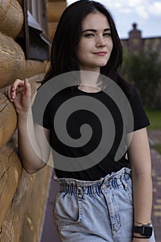 Attractive young brunette woman in black t-shirt and denim shorts next to a wooden modern house