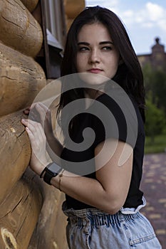 Attractive young brunette woman in black t-shirt and denim shorts next to a wooden modern house