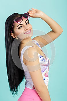 Attractive young brunette woman in pink tank top on blue background. smilling girl in sunglasses