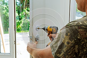 Attractive young builder is installing lock in door. He is holding a screwdriver and kneeling.