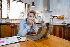 Attractive young business man on computer working from home feeling stressed, tired and overwhelmed