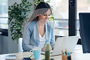 Attractive young business woman working with computer while  sitting in desk in modern startup office