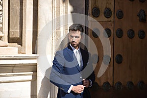 Attractive young businessman with beard and suit, holding lapels of jacket leaning against a wall with face half light and half photo