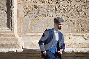 Attractive young businessman with beard and suit, posing leaning against a stone wall. Concept beauty, fashion, success, achiever