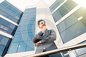 Attractive young businessman with hands on chin in front of a modern office building on a beautiful sunny day.