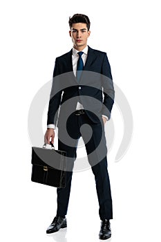 attractive young businessman holding bag and posing with hand in pocket