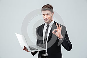 Attractive young businessman holding laptop and showing ok sign