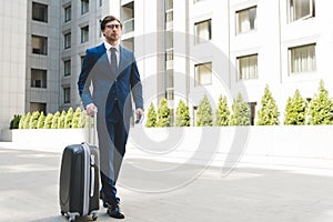 attractive young businessman in stylish suit with luggage walking