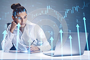 Attractive young businesswoman at desk with laptop and growing blue vertical arrows and candlestick forex chart on blurry index